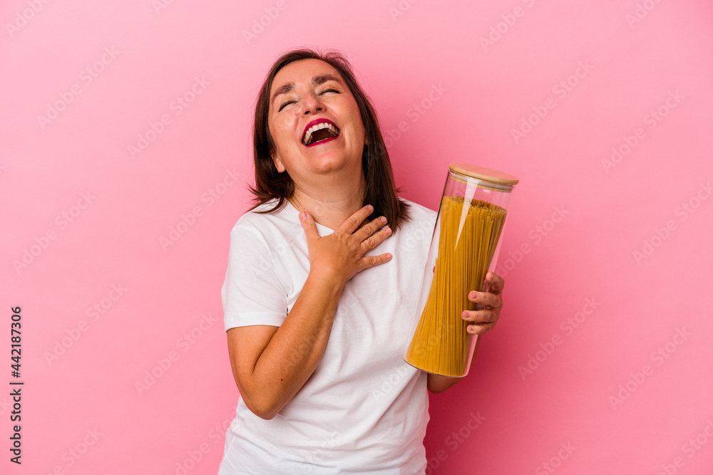 Middle age caucasian woman holding a pasta jar isolated on pink background laughs out loudly keeping hand on chest. Middle age caucasian woman holding a pasta jar isolated on pink background laughs out loudly keeping hand on chest.