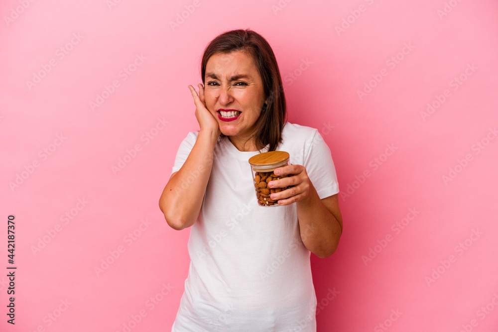 Middle age caucasian woman holding an almond jar isolated on pink background covering ears with hands. Middle age caucasian woman holding an almond jar isolated on pink background covering ears with hands.