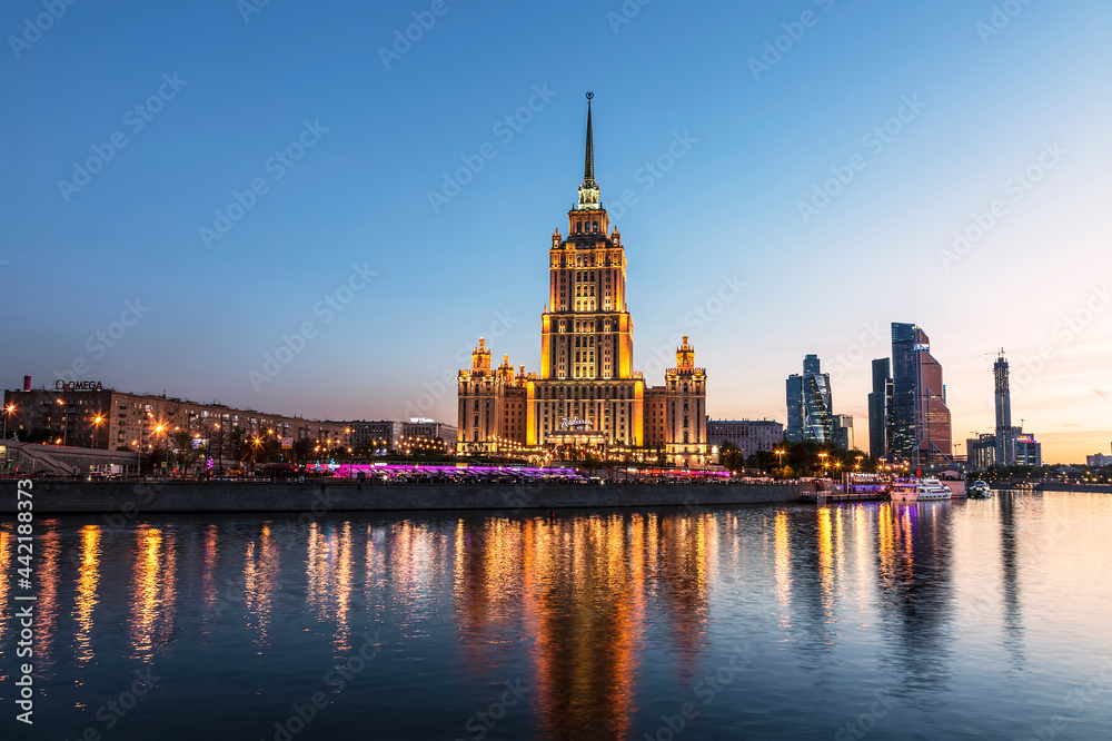 Fototapeta premium View of the Taras Shevchenko Embankment with the building of the hotel Ukraine (Radisson Royal Hotel, Moscow) and the Moscow River in the evening illumination. Moscow, Russia