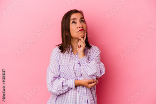 Middle age caucasian woman isolated on pink background thinking and looking up, being reflective, contemplating, having a fantasy. © Asier