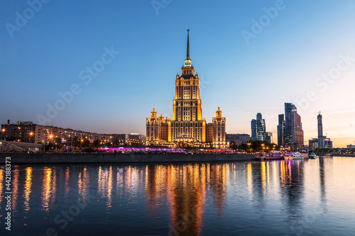 View of the Taras Shevchenko Embankment with the building of the hotel Ukraine (Radisson Royal Hotel, Moscow) and the Moscow River in the evening illumination. Moscow, Russia