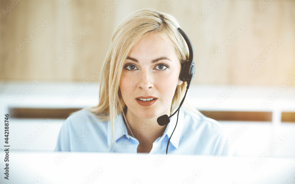 Blonde business woman sitting and communicated by headset in call center in sunny office. Concept of telesales business Blonde business woman sitting and communicated by headset in call center in sunny office. Concept of telesales business