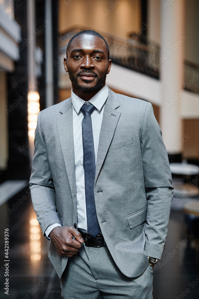 Vertical portrait o successful African-American businessman looking at camera while standing at luxurious hotel lobby