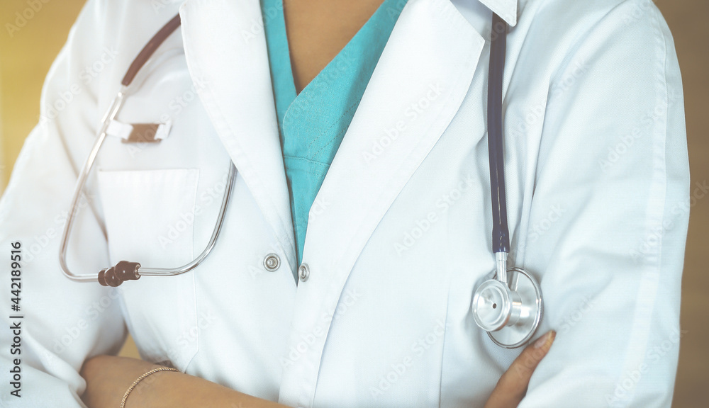 Unknown female doctor standing with arms crossed in sunny clinic, close-up Unknown female doctor standing with arms crossed in sunny clinic, close-up