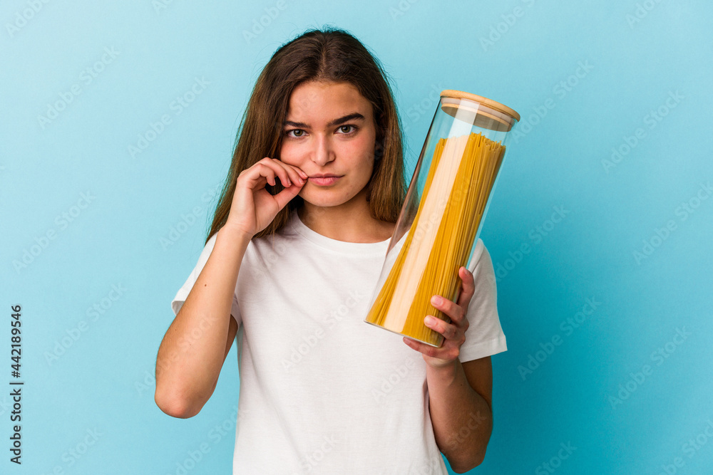 Young caucasian woman holding a pasta jar isolated on blue background with fingers on lips keeping a secret. Young caucasian woman holding a pasta jar isolated on blue background with fingers on lips keeping a secret.