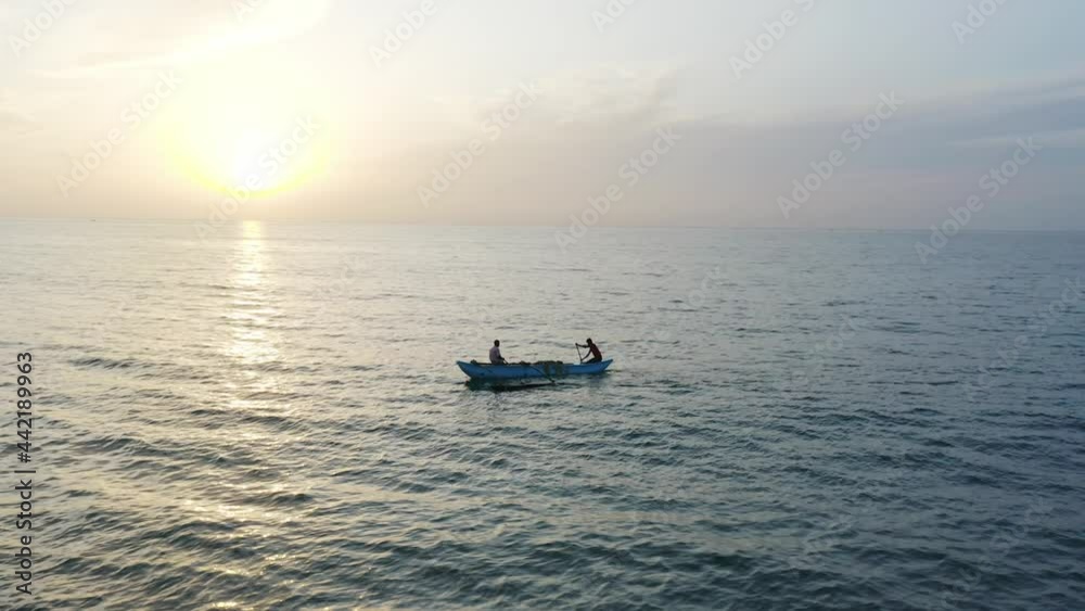 Fisherman in wooden catamaran paddling in calm sea during sunrise, aerial Fisherman in wooden catamaran paddling in calm sea during sunrise, aerial