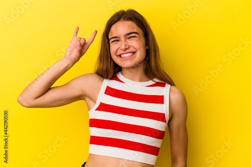 Young caucasian woman isolated on yellow background showing rock gesture with fingers © Asier