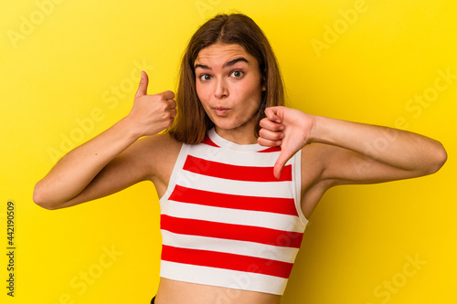 Young caucasian woman isolated on yellow background showing thumbs up and thumbs down, difficult choose concept © Asier