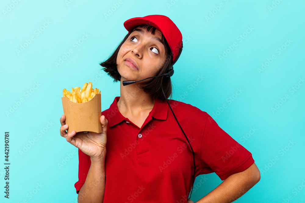 Young mixed race woman fast food restaurant worker holding fries isolated on blue background dreaming of achieving goals and purposes Young mixed race woman fast food restaurant worker holding fries isolated on blue background dreaming of achieving goals and purposes