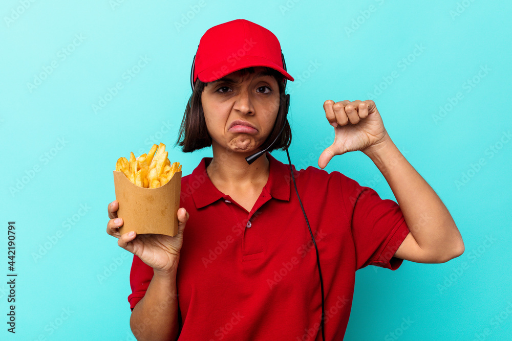 Young mixed race woman fast food restaurant worker holding fries isolated on blue background showing a dislike gesture, thumbs down. Disagreement concept.