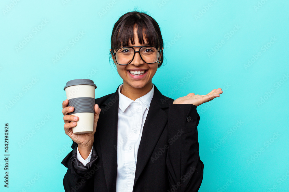 Young business mixed race woman holding a coffee isolated on blue background showing a copy space on a palm and holding another hand on waist. Young business mixed race woman holding a coffee isolated on blue background showing a copy space on a palm and holding another hand on waist.