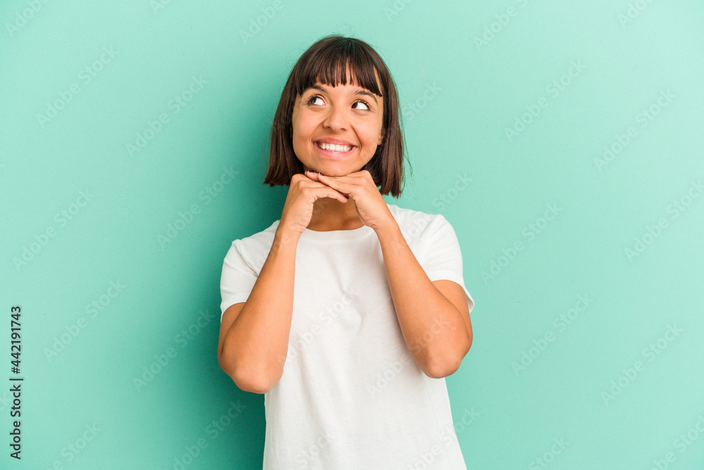 Young mixed race woman isolated on blue keeps hands under chin, is looking happily aside. Young mixed race woman isolated on blue keeps hands under chin, is looking happily aside.