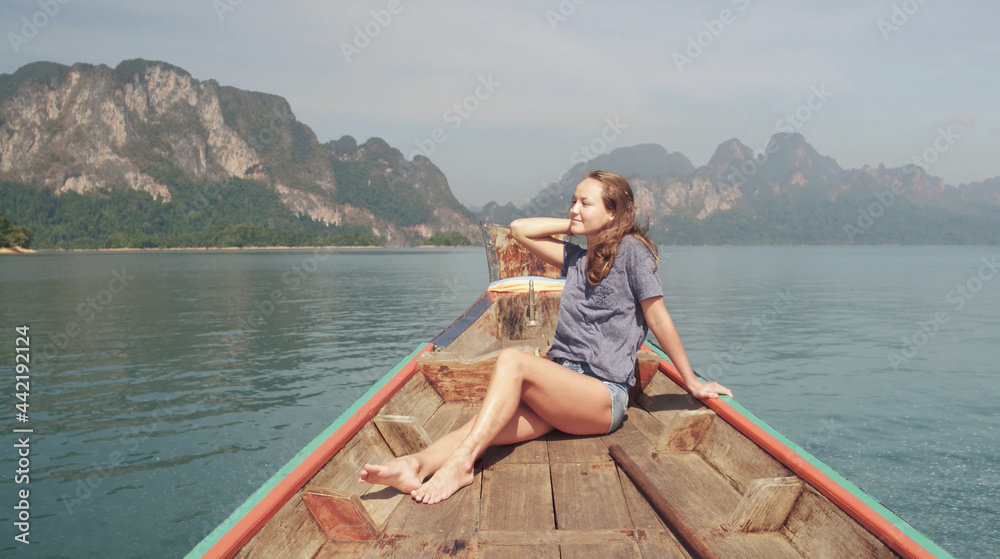 Young Happy Mixed Race Girl Sitting and Relaxing on Traditional Thai Wooden Long Tail Boat at Khao Sok Lake. Phang Nga Province, Thailand.