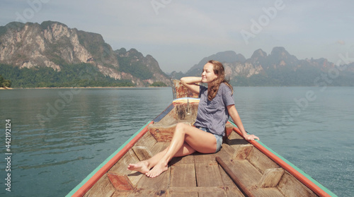 Young Happy Mixed Race Girl Sitting and Relaxing on Traditional Thai Wooden Long Tail Boat at Khao Sok Lake. Phang Nga Province, Thailand.