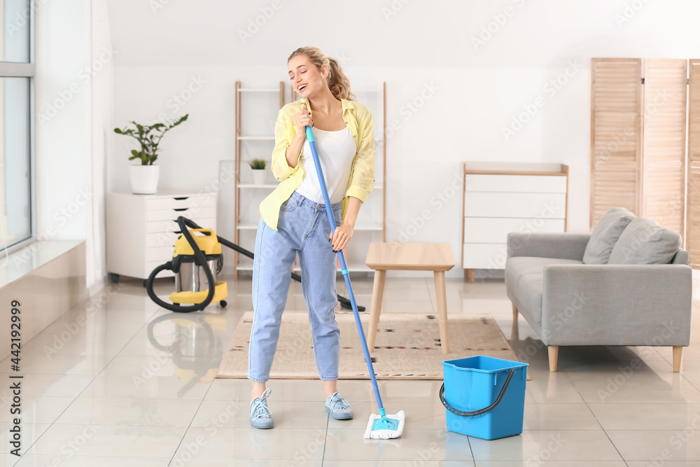 Young woman having fun while mopping floor in her flat Young woman having fun while mopping floor in her flat