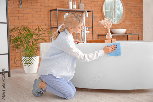 Young woman cleaning bath tube in bathroom photo