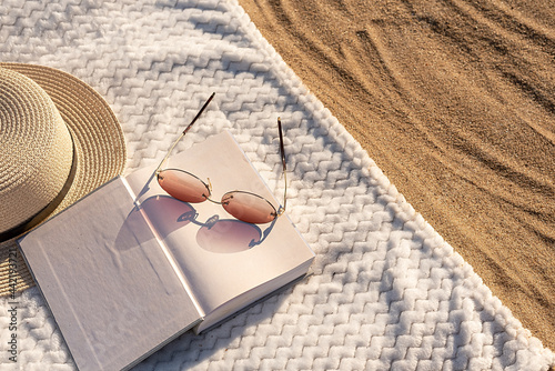Summer vacation on the beach on the sand. On a white towel book glasses and a hat.