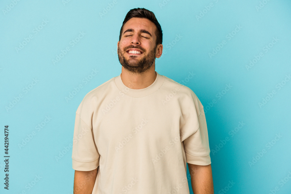 Young caucasian man isolated on blue background laughs and closes eyes, feels relaxed and happy. Young caucasian man isolated on blue background laughs and closes eyes, feels relaxed and happy.