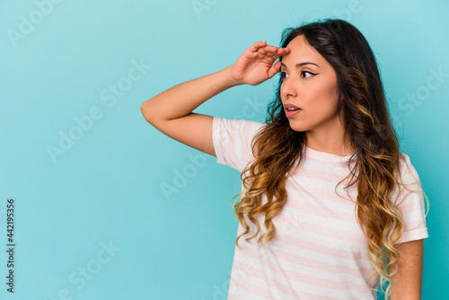 Young mexican woman isolated on blue background looking far away keeping hand on forehead.