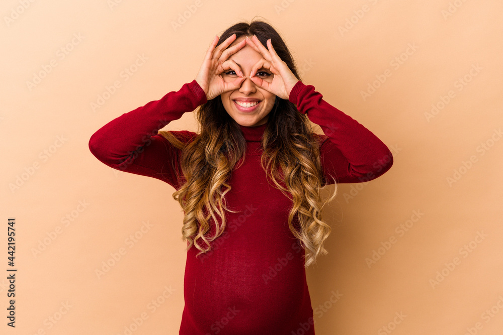 Young mexican pregnant woman isolated on beige background showing okay sign over eyes Young mexican pregnant woman isolated on beige background showing okay sign over eyes