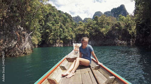 Young Happy Mixed Race Girl Sitting and Relaxing on Traditional Thai Wooden Long Tail Boat at Khao Sok Lake. Phang Nga Province, Thailand. © skymediapro