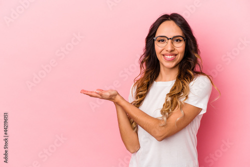 Young mexican woman isolated on pink background holding a copy space on a palm.
