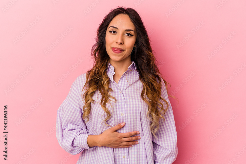 Fototapeta premium Young mexican woman isolated on pink background touches tummy, smiles gently, eating and satisfaction concept.