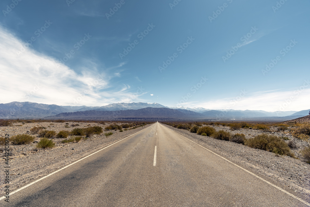 two lane road in a arid landscape in Argentina leading to mountains against blue sky