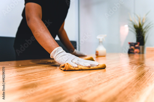 Hand of waiter woman cleaning table with disinfectant spray and microfiber cloth for disinfecting at indoor restaurant. Coronavirus prevention concept.