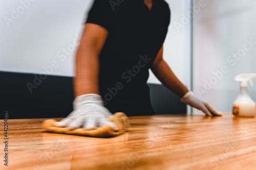 Hand of waiter woman cleaning table with disinfectant spray and microfiber cloth for disinfecting at indoor restaurant. Add movement filter effect. Coronavirus prevention concept.