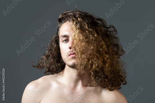 Man with long curly hair, haircut, modern hair style. Close up portrait of male model with long hair. Healthcare and hair care concept.