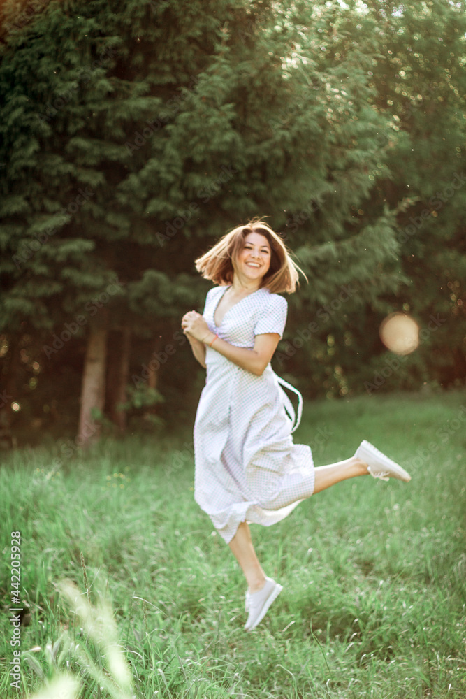 A beautiful happy girl in a long white dress jumps up in the meadow and laughs. Selective focus. Vintage photo