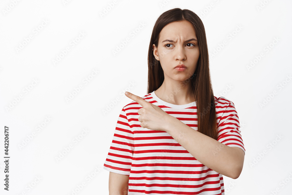 Suspicious girl squinting, pointing and looking left with doubtful uspet face, express disbelief, standing in tshirt against white background Suspicious girl squinting, pointing and looking left with doubtful uspet face, express disbelief, standing in tshirt against white background