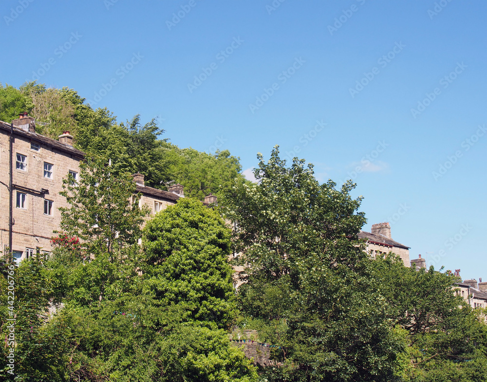 a row of traditional tall houses on a hillside surrounded by trees in summer in hebden bridge west yorkshire
