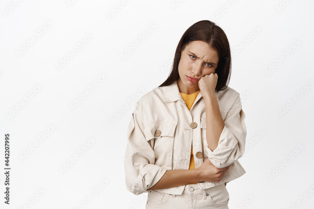 Image of silly moody girl, sulking and furrow eyebrows, lean face on fist, complaining, looking displeased at smth unfair, dislike situation she stuck in, white background Image of silly moody girl, sulking and furrow eyebrows, lean face on fist, complaining, looking displeased at smth unfair, dislike situation she stuck in, white background