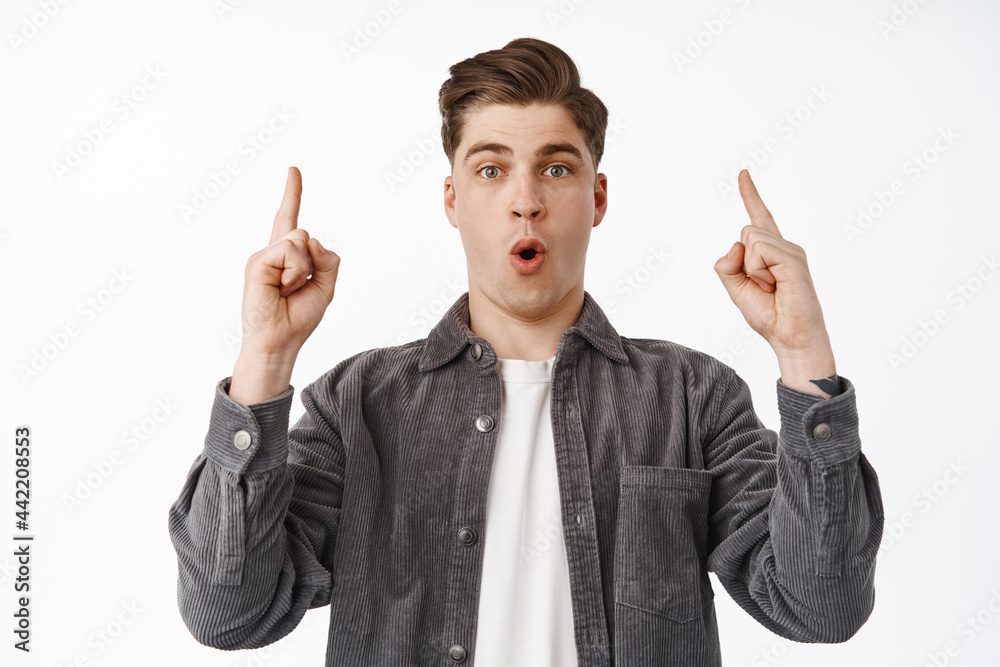 Imressed young man checking out big discounts in store, pointing fingers up and gasping, saying wow excited about advertisement special deal, white background Imressed young man checking out big discounts in store, pointing fingers up and gasping, saying wow excited about advertisement special deal, white background