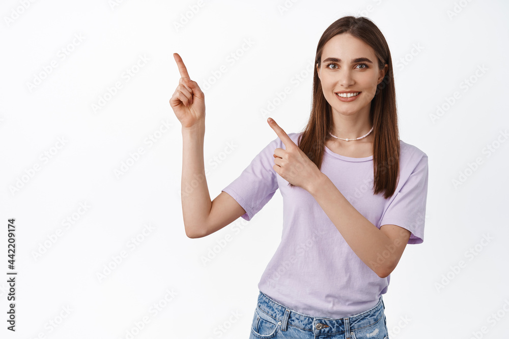 This way. Smiling girl friendly pointing left, showing advertisement, direction to banner or promotonal text against empty white space, studio background This way. Smiling girl friendly pointing left, showing advertisement, direction to banner or promotonal text against empty white space, studio background