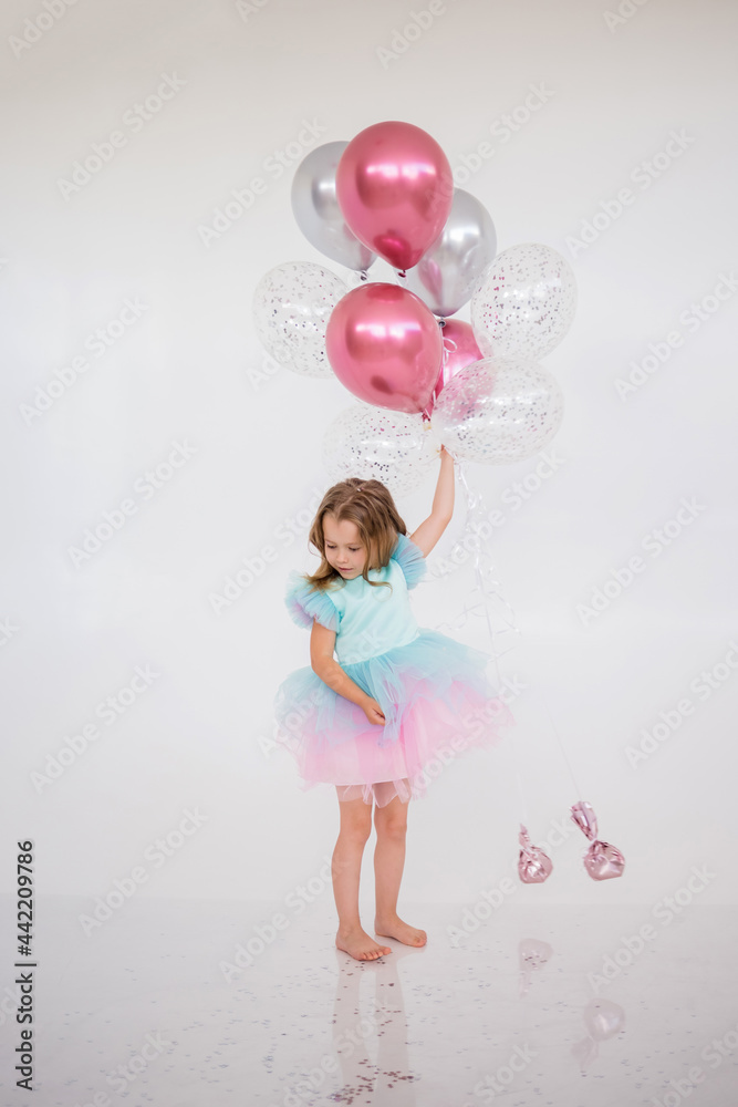 Fototapeta premium little girl in a festive dress stands with a bunch of balloons on white with a place for text