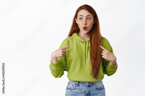 Amazed ginger girl gasp and say wow, pointing at herself and looking at logo aside, self-promoting, asking to pick her, wants to volunteer, white background