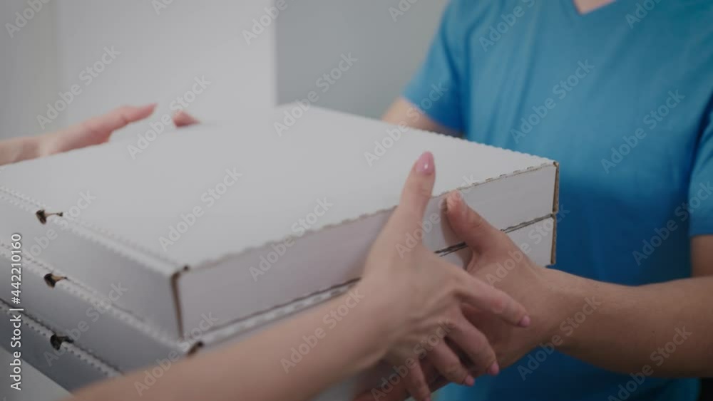 A food delivery man hands over the order to a woman. Close-up of pizza boxes and food packages. A food delivery man hands over the order to a woman. Close-up of pizza boxes and food packages.