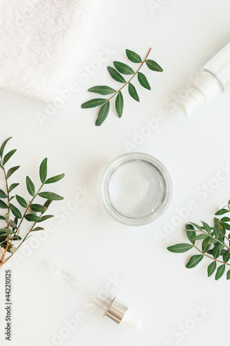 A jar of moisturizing body cream, a bath towel, sprigs of herbs, a bottle of serum, a dropper. Skin care cosmetic concept. Flat lay style minimal composition, top view, copy space