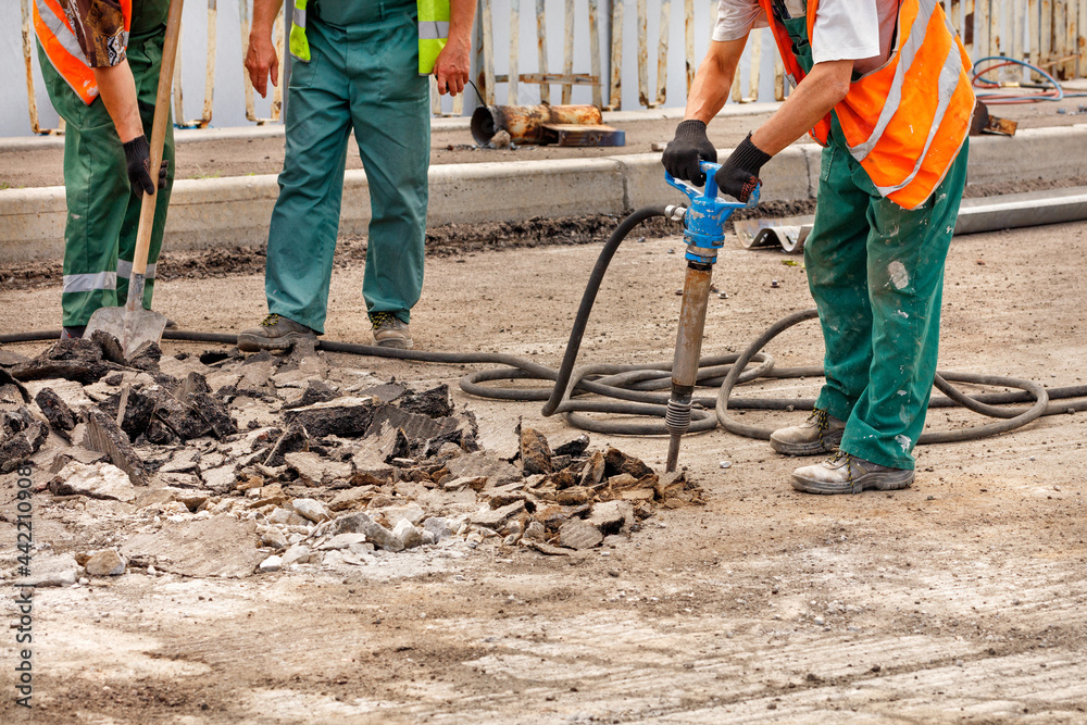 A team of road workers are repairing a section of road by smashing old asphalt with a pneumatic jackhammer.