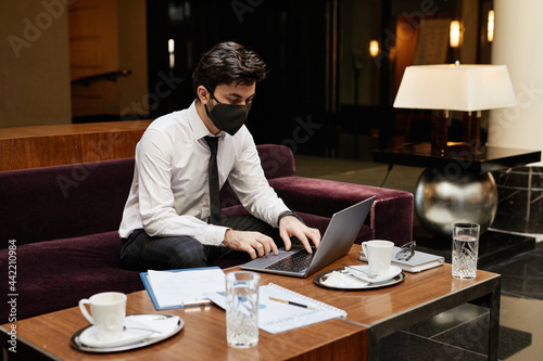 Portrait of young businessman wearing mask while working in hotel lobby, copy space