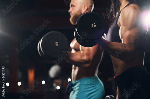 Strong man and muscled woman lifting weights at the gym