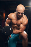 Well-shaped male athlete doing exercises with dumbbells