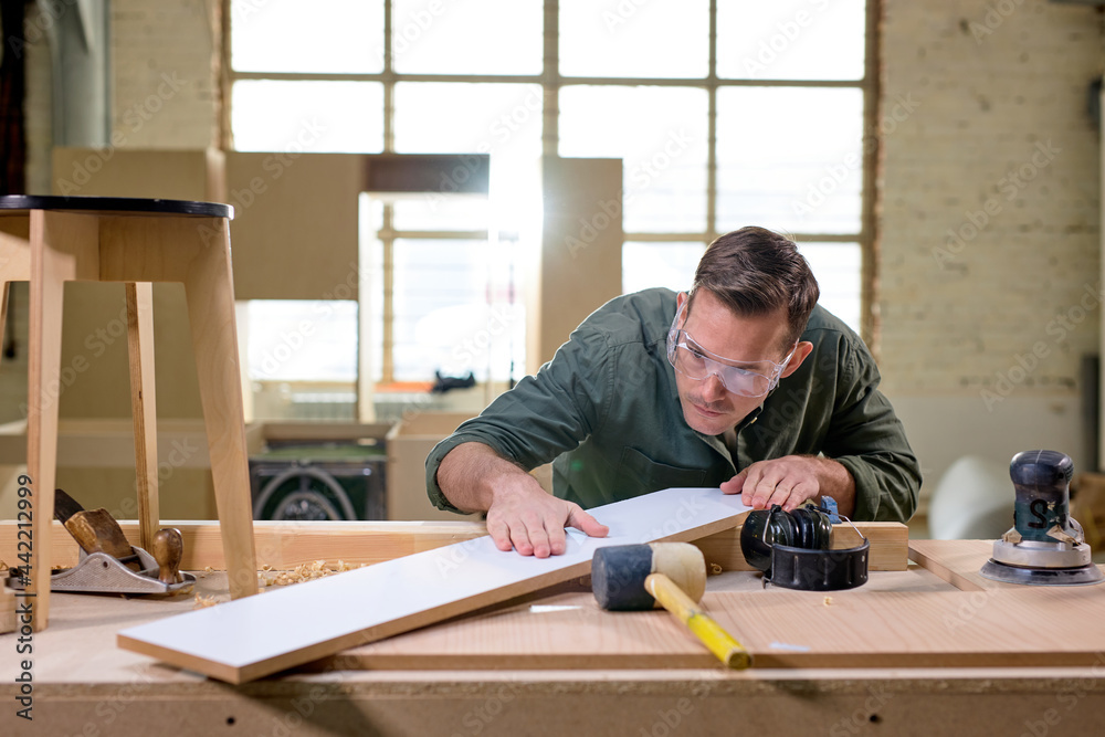 Professional joiner comparing, checking the length and surface of wooden material looking confident. carpenter works in joinery, workshop for woodworking and sawing Professional joiner comparing, checking the length and surface of wooden material looking confident. carpenter works in joinery, workshop for woodworking and sawing