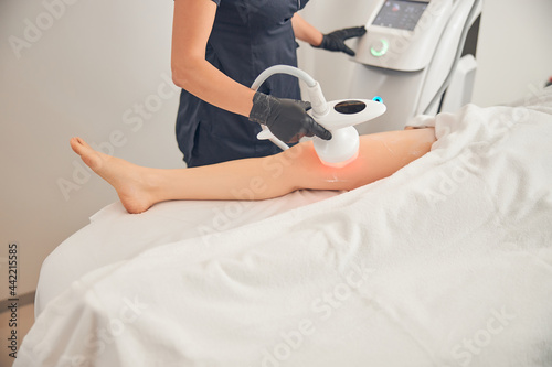 Cosmetologist reducing cellulite on the legs of a female patient