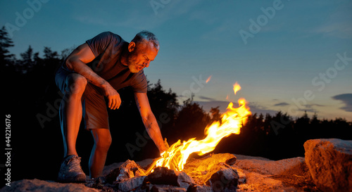 Middle aged man, tourist making a fire in the wild at dusk