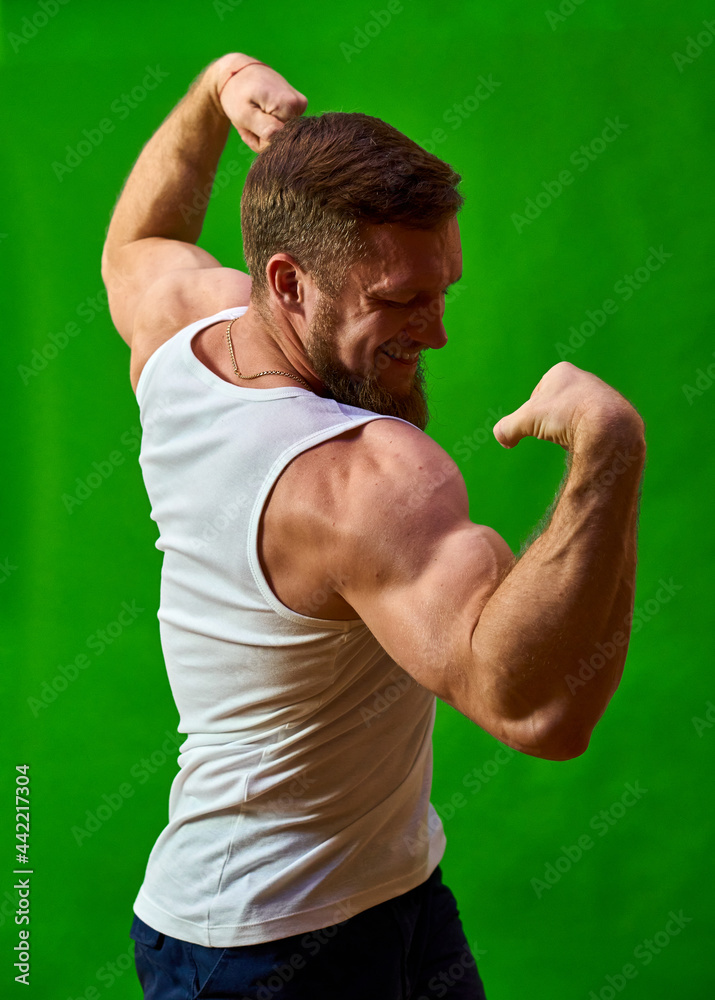 Bodybuilder posing. Young athlete and muscular athlete shows shape. Caucasian man with a beard on a green background. Strong Men Flexing Back. show muscles development Space for text and advertising. Bodybuilder posing. Young athlete and muscular athlete shows shape. Caucasian man with a beard on a green background. Strong Men Flexing Back. show muscles development Space for text and advertising.