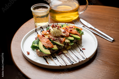 Healthy dietical snack in a cafe: salmon and avocado toast with a fresh poached egg, served with a pot of green tea photo